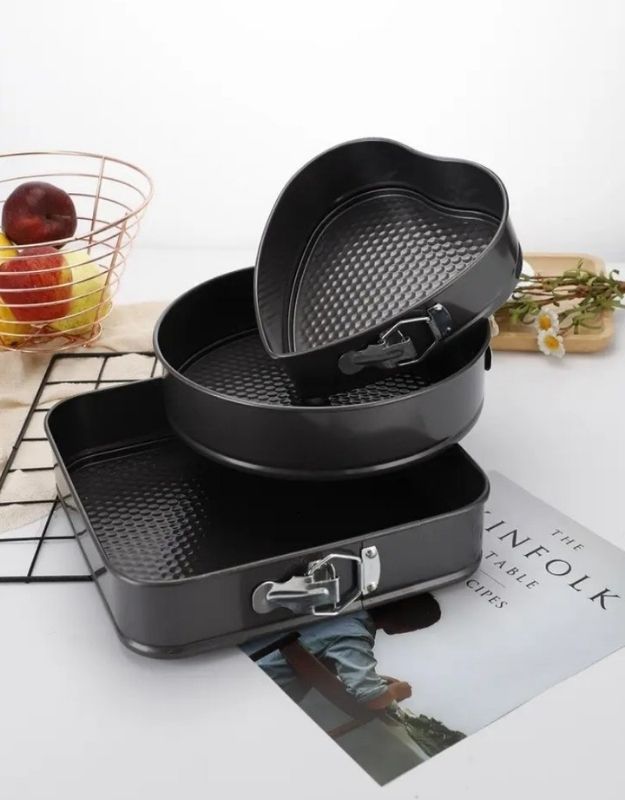 Set of black cookware pieces on a magazine with a white background. Set of nonstick springform cake pans in round, square, and heart shape with latch design.